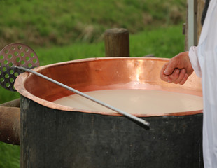 cheesemaker checks with hand the milk's temperature inside the b