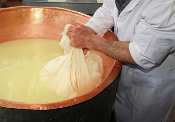 herdsman Cheesemaker collects cheese from the  copper cauldron w