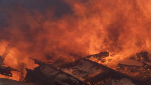 Flames raging above the collapsed wall of a burning house fill the frame