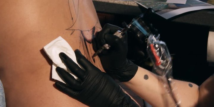 Close-up of an artist's hands inking a tattoo onto a woman's back