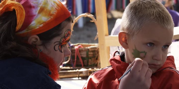 Artist painting a design on a little boy's face at a fair
