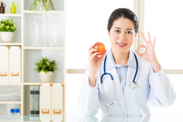 Young asian nutritionist recommend eating apple and ok sign