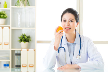 Young asian nutritionist eating a orange