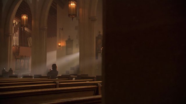 Woman kneeling and praying in sunlit nave of a Catholic church