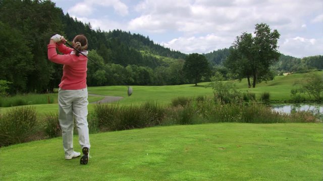 Woman golfer teeing off and hitting ball down fairway, watching its flight
