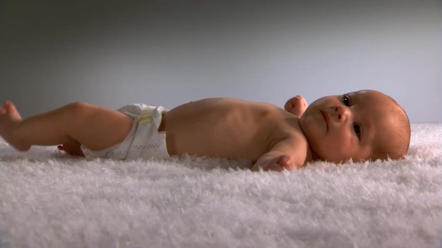 Baby In Diaper Lying On Fluffy Blanket, Kicking And Flexing Limbs Contentedly