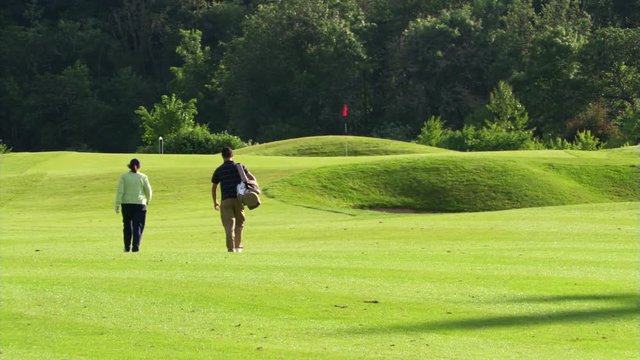 Rear view of woman golfer and her caddy walking down fairway toward flag