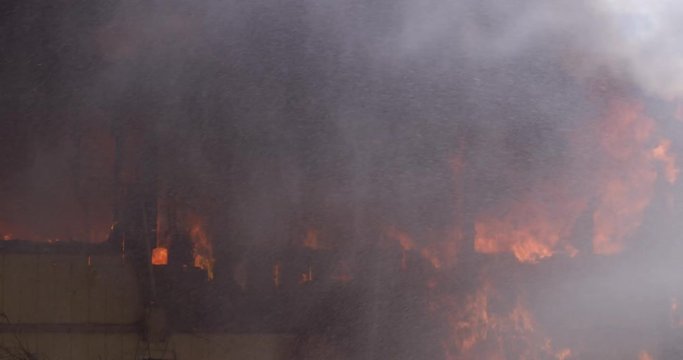 Spray from an out of frame hose falls on the blazing remains of a burning house