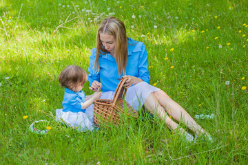 Little girl with her mother and a basket on a picnic in the grass