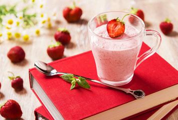 Strawberry mousse in a transparent mug on a light background with books, strawberries and chamomile flowers 