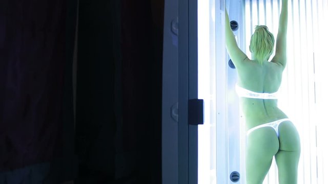 beautiful girl stands in the solarium and sunbathing in the rays