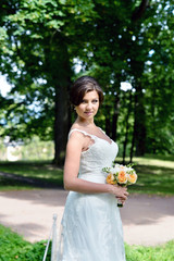 Beauty bride in bridal gown with bouquet and lace veil on the nature. Beautiful model girl in a white wedding dress. Female portrait in the park. Woman with hairstyle. Cute lady outdoors