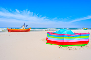 Fishing boats and colorful windbreaker with tent on sandy Baltic Sea beach, Poland