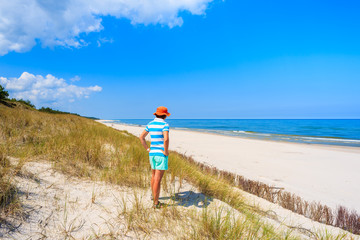 Young woman tourist standing on sand dune and looking at white sand beach in Bialogora, Baltic Sea, Poland
