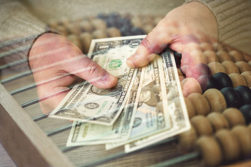 hands counting dollars banknotes against the backdrop of ancient accounts (abacus). Double exposure, photomontage © Yuli