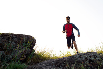 Naklejka na ściany i meble Young Sportsman Running on the Rocky Mountain Trai in the Evening. Active Lifestyle