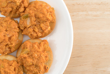 Spicy chicken salad on butter crackers top view on a white plate atop a wood table.