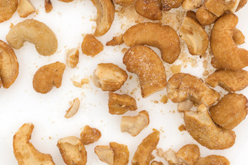 Pieces of honey roasted cashews on a white plate top close view.