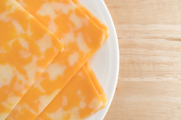 Colby-Jack cheese slices top close view on a plate atop a wood table.