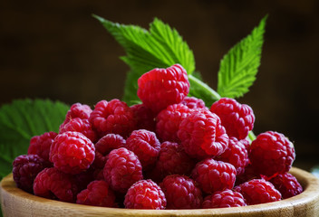 Fresh organic raspberries in bowl, green leaves, vintage wooden