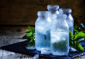 Tuinposter Water Zeer koud mineraalwater met ijs in een beslagen glazen flessen, donker