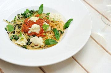 The image is very tasty spaghetti bolognese with cheese and basil on a white table.