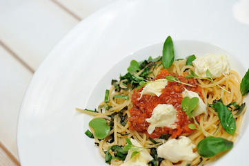 The image is very tasty spaghetti bolognese with cheese and basil on a white table.