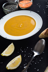 Cream soup of assorted lentil. Yellow and green lens, spices as raw for meal and lemon on black background. Healthy, appetizing, delicious, vegetarian food. Top view, copy space.
