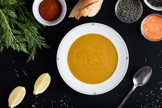 Cream soup of assorted lentil. Yellow and green lens, spices as raw for meal and lemon on black background. Healthy, appetizing, delicious, vegetarian food. Top view, copy space.
