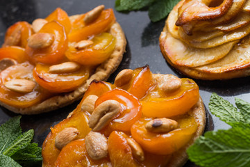 Tart with apricot and apple. Traditional french pie with fruits on dark marble background. Decorated almonds and mint leafs. Delicious dessert with copy space closeup.
