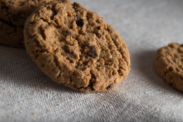 Cookies pile with chocolate chip on light textile background. Delicious morning snacks for breakfast, brunch and lunch. Appetizing, healthy, sweet, scrummy, and fast food.