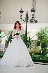 Fototapeta premium Portrait of charming red-haired bride model with wedding bouquet