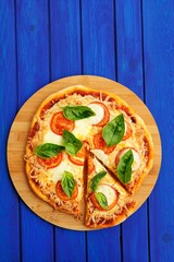 Cutted margherita pizza with basil on blue background with copyspace