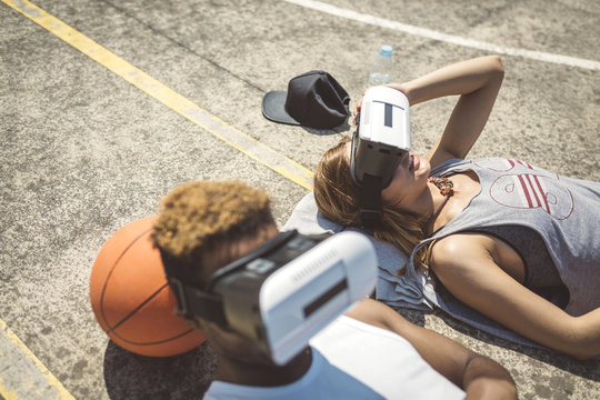 Young couple using virtual reality glasses, resting heads on basketball