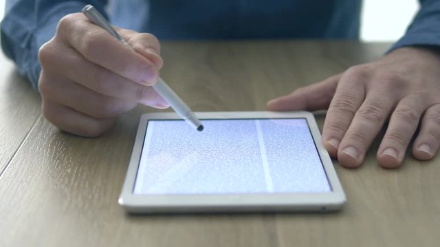 Man reading an ebook on a digital touch screen tablet, he is using a stylus, hands close up
