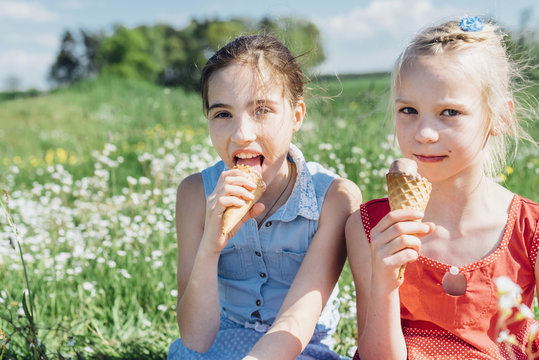 Two girls in meadow eating ice cream cones
