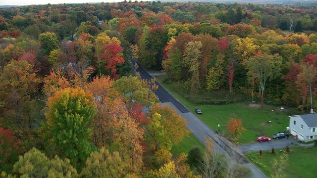 Flying over rural New England neighborhood among autumn woods