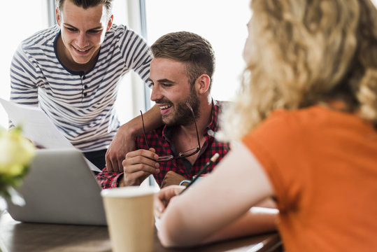 Smiling young professionals sharing laptop in office