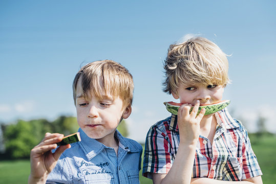 Two boys outdoors eating watermelon
