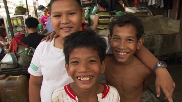 Group portrait of three smiling Cambodian boys at a street market