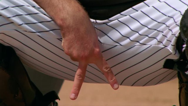 Close-up of catcher's legs and lower body as he gives hand signals to the pitcher