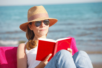 Relaxing on the beach. Beautiful woman reading a book at seaside. 