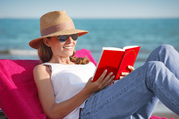 Relaxing on the beach. Beautiful woman reading a book at seaside. 