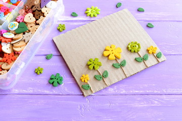Fun card with flowers. Flowers buttons and leaves on lilac wooden background. Plastic box with...