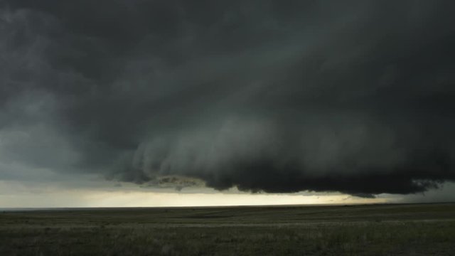 Low dark wall cloud with striations spreading over prairie landscape, time lapse
