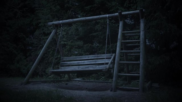 Empty wooden swing with ladder moving at night.