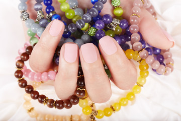 Hand with beige matte manicured nails and colorful bracelets