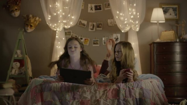 Medium shot of teenage girls sharing digital tablet in bedroom / Cedar Hills, Utah, United States