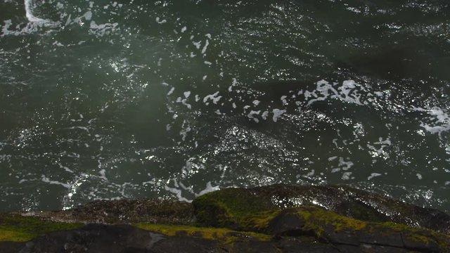 Looking down on Pacific waves surging around a mossy rock