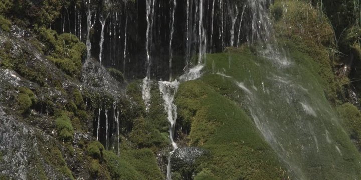 Water trickling from an unseen ledge and flowing over moss-covered boulders